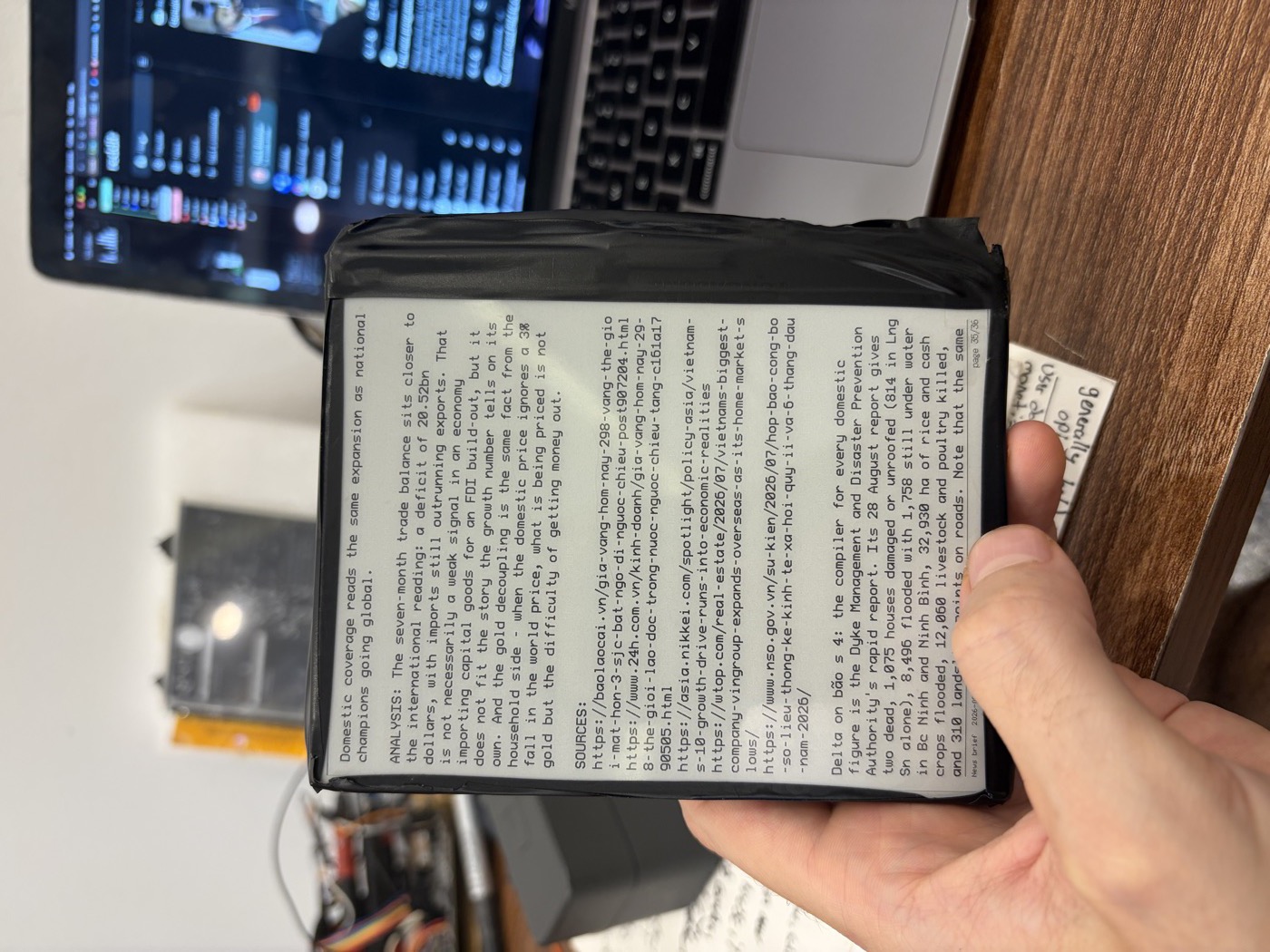 Handheld e-paper reader in a taped case showing a page of a generated news brief.